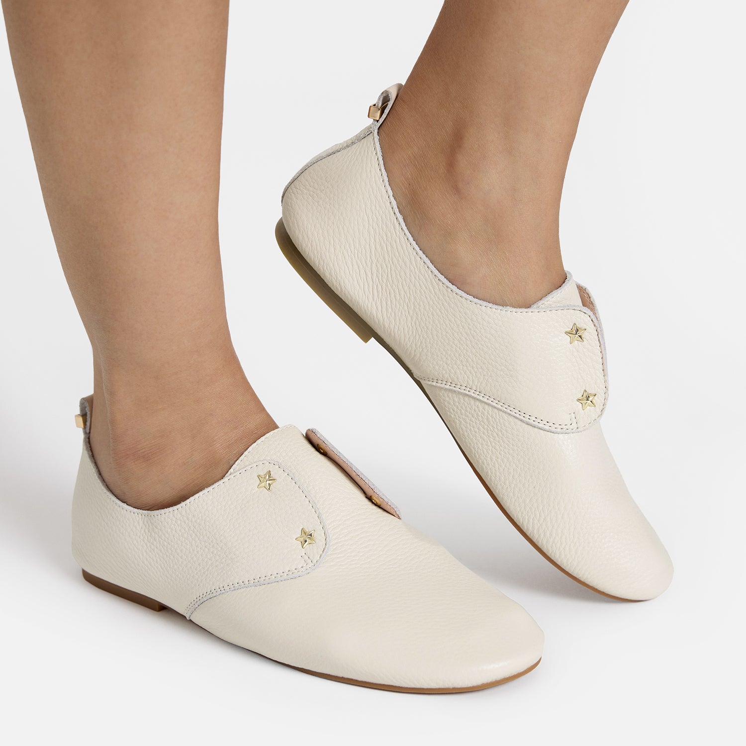 Xeno ivory slip on house shoe with gold star studs shown on women's feet.